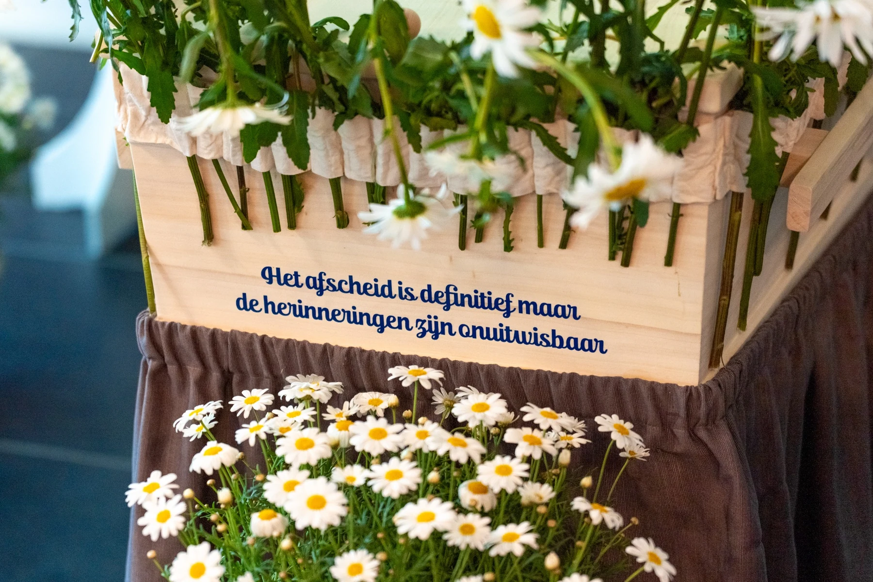 Bloemen en een persoonlijke tekst op een houten uitvaartkist